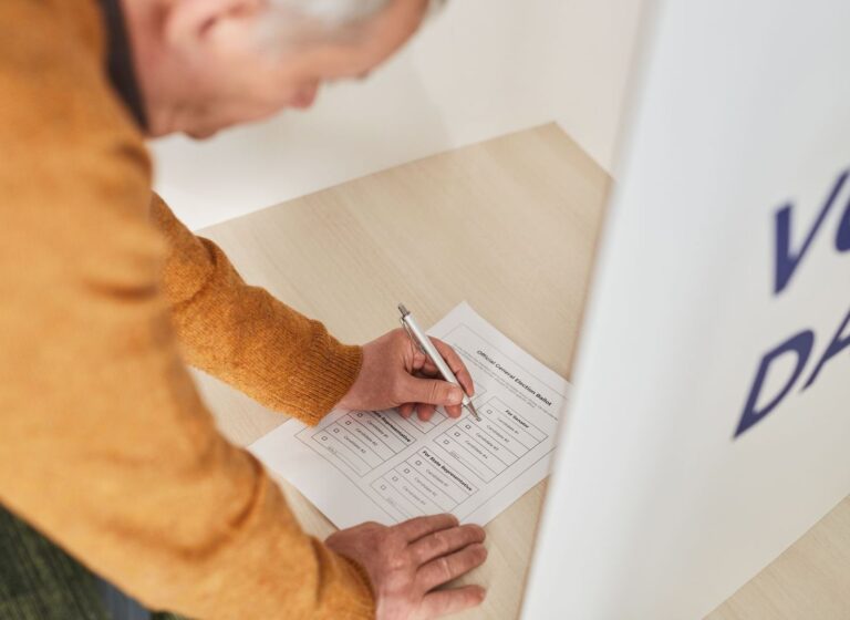 An older voter filling out an official election ballot paper in a voting booth.