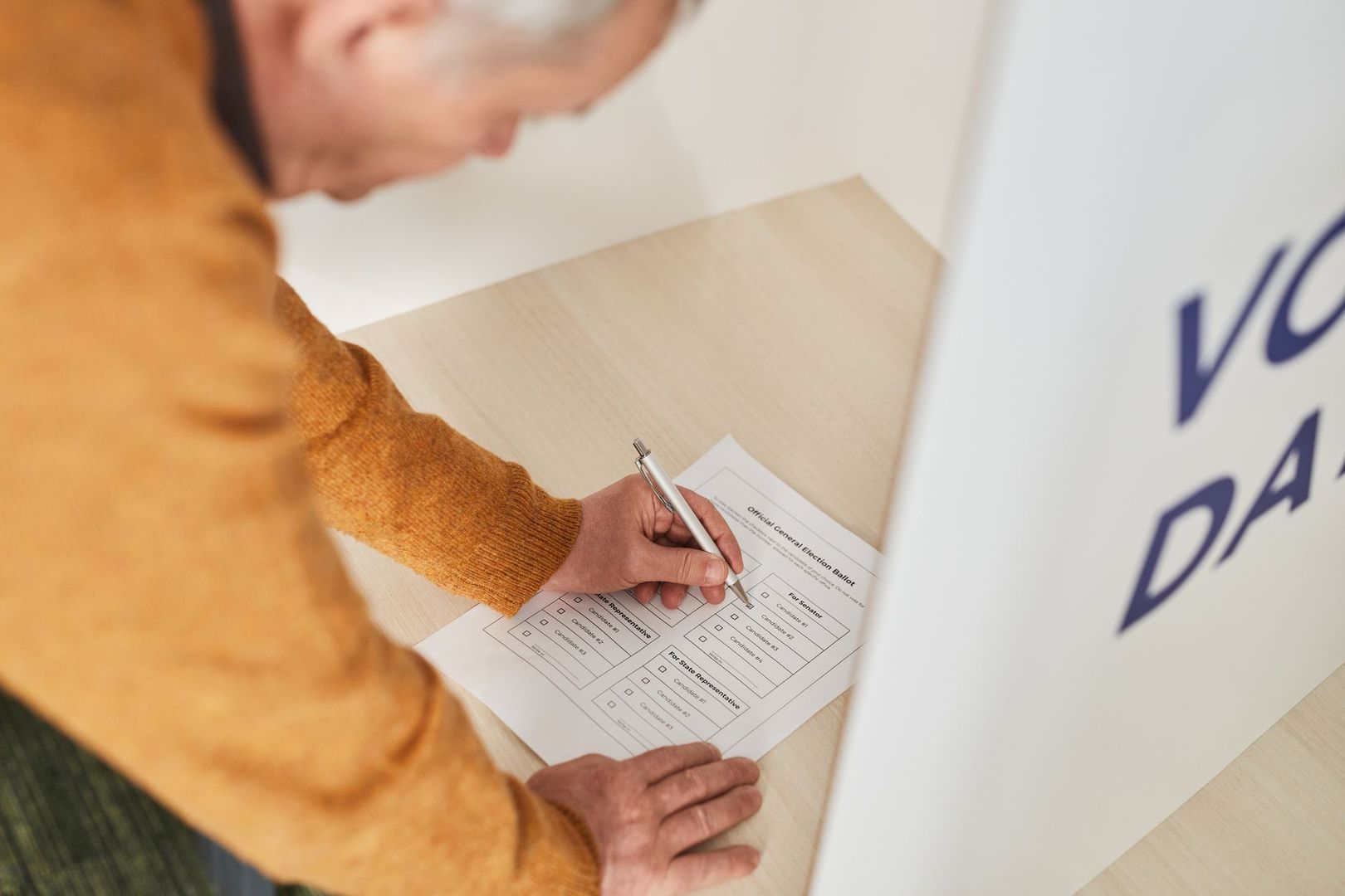 An older voter filling out an official election ballot paper in a voting booth.